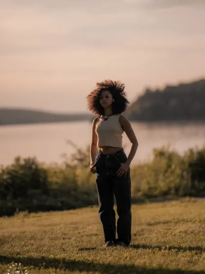 Model with curly hair backlit by a low sun in a park by the water