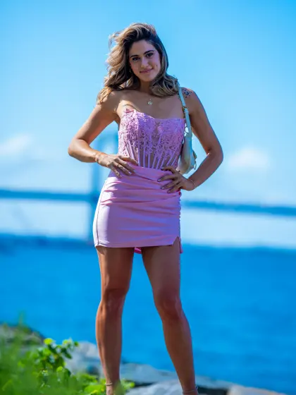 Model in a pink dress standing by the water under a clear blue sky