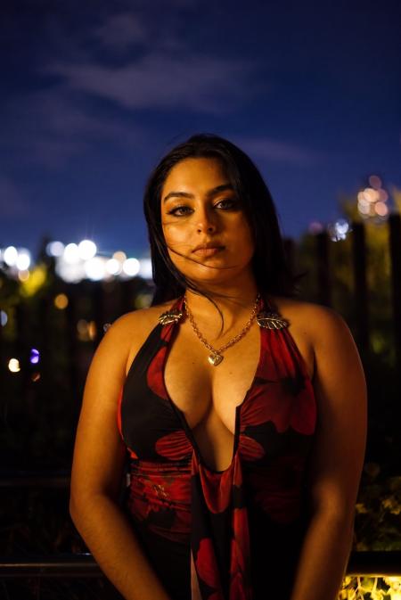 Portrait of a woman in a red and black dress against a dusk sky and blurred city lights