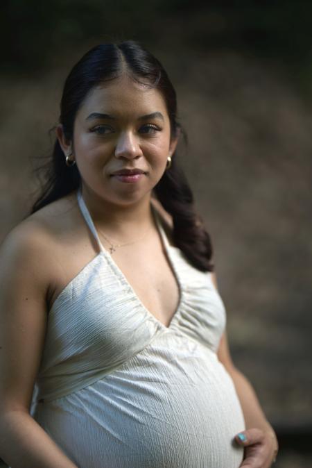 Portrait of an expecting mother in a white halter dress against a soft green background
