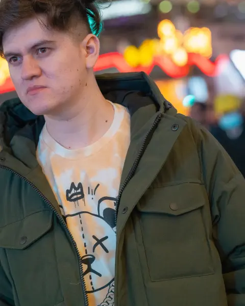 Young man in an olive parka on a lit-up city street at night