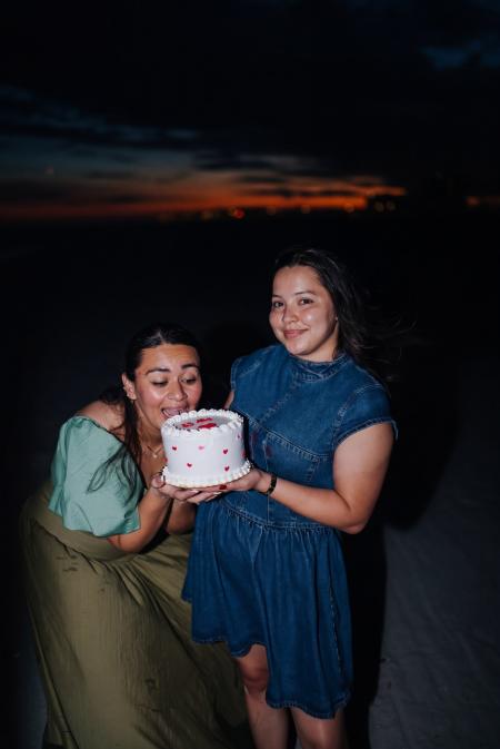 Two friends sharing a small birthday cake on the beach at night