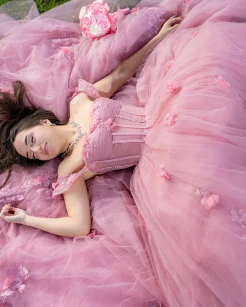 Quinceañera in a pink tulle gown lying back on the grass