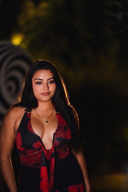 Close portrait of a woman with long dark hair in a red dress, warm light behind her at night