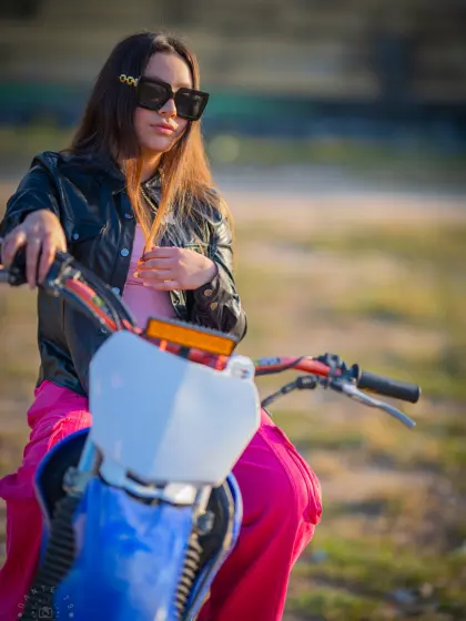 Model in sunglasses and a leather jacket astride a blue dirt bike