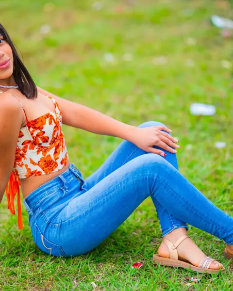 Woman in an orange top and jeans sitting on the grass in the sun