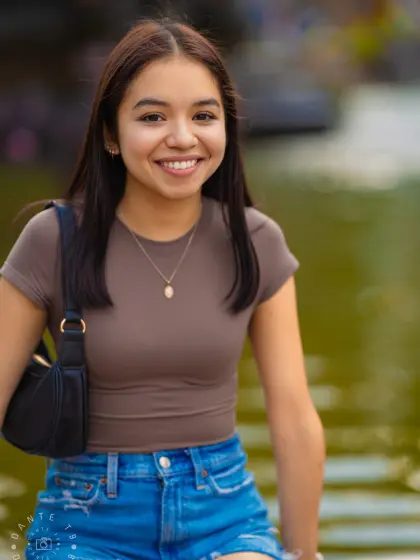 Smiling model in a brown top sitting beside a pond