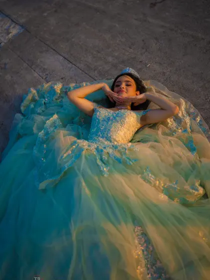 Quinceañera in a teal ball gown lying on stone steps in warm evening light