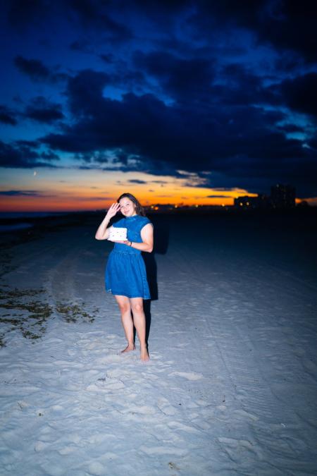 Woman holding a birthday cake on the beach under a deep blue sunset sky
