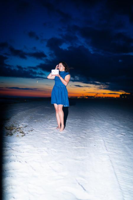 Woman with a birthday cake on the beach with an orange sunset glowing on the horizon