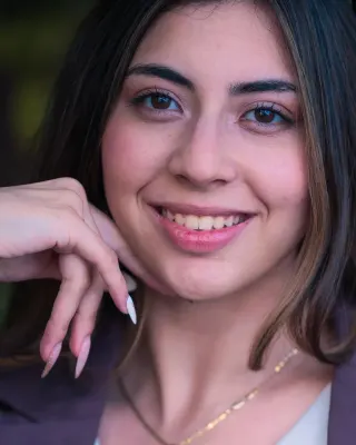 Smiling young woman in a plum blazer, hand resting near her chin