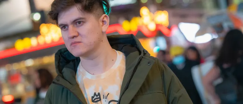 Young man in an olive parka on a neon-lit New York street at night