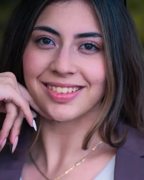 Portrait of a smiling young woman with long dark hair, one hand raised to her face